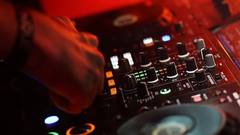 DJ hand on a mixer channel strip lit in red inside a club booth