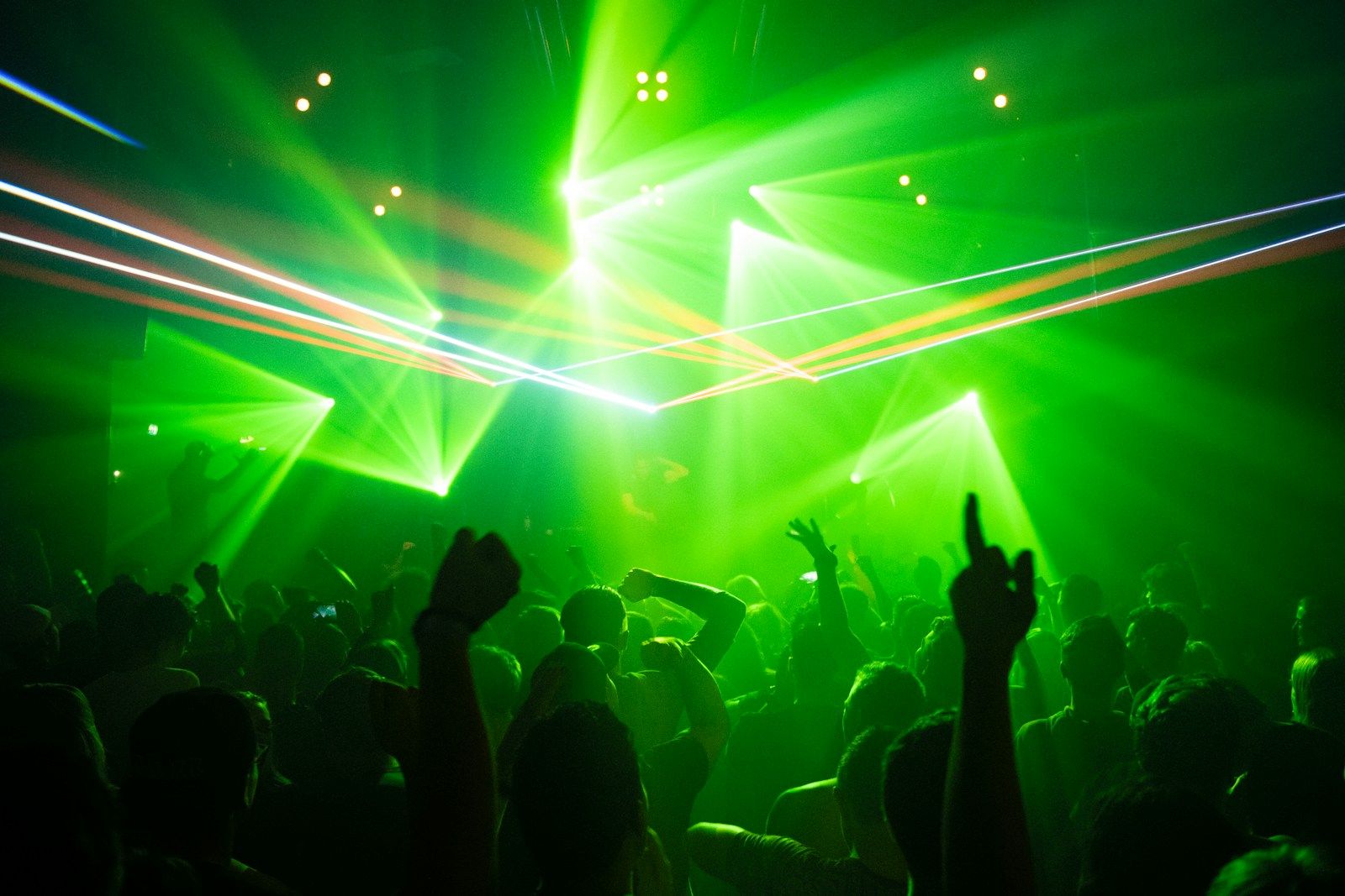 Dark club interior with green stage lighting and crowd in motion