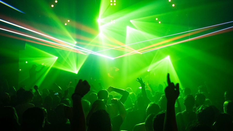 Dark club interior with green stage lighting and crowd in motion