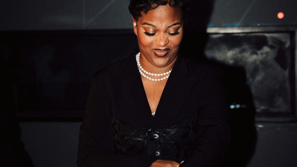 Female DJ performing at a nighttime event, working at a booth in a dark venue with warm lighting