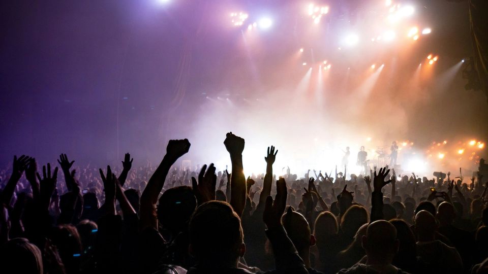 A crowd at a dark nighttime electronic music event, coloured lights overhead