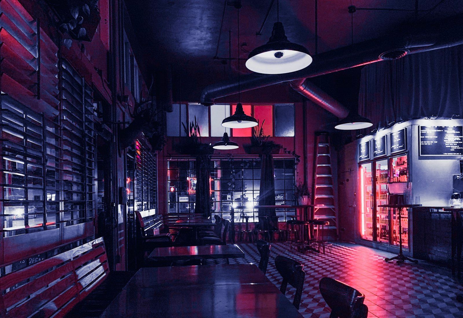 A dark, empty bar with pendant lamps, a checkered floor and red neon glow after closing time