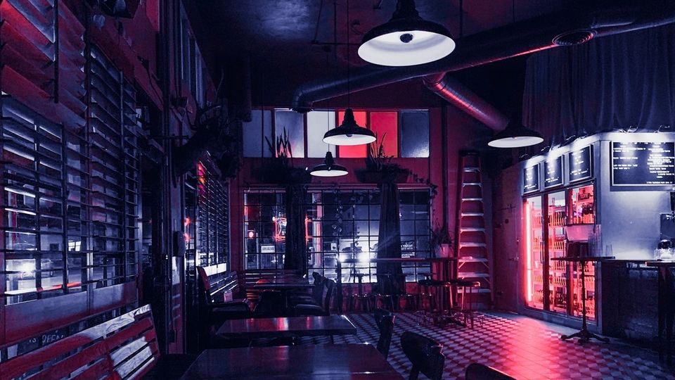 A dark, empty bar with pendant lamps, a checkered floor and red neon glow after closing time