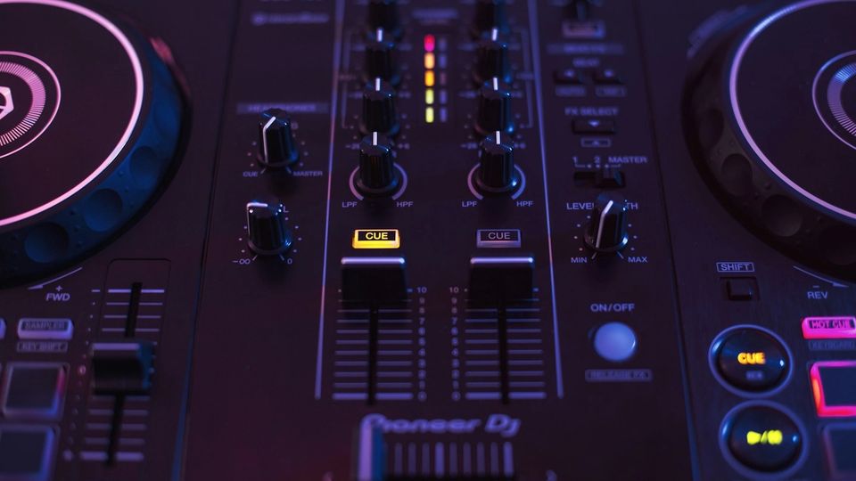 Close-up of a Pioneer DJ controller showing channel faders in dark studio lighting