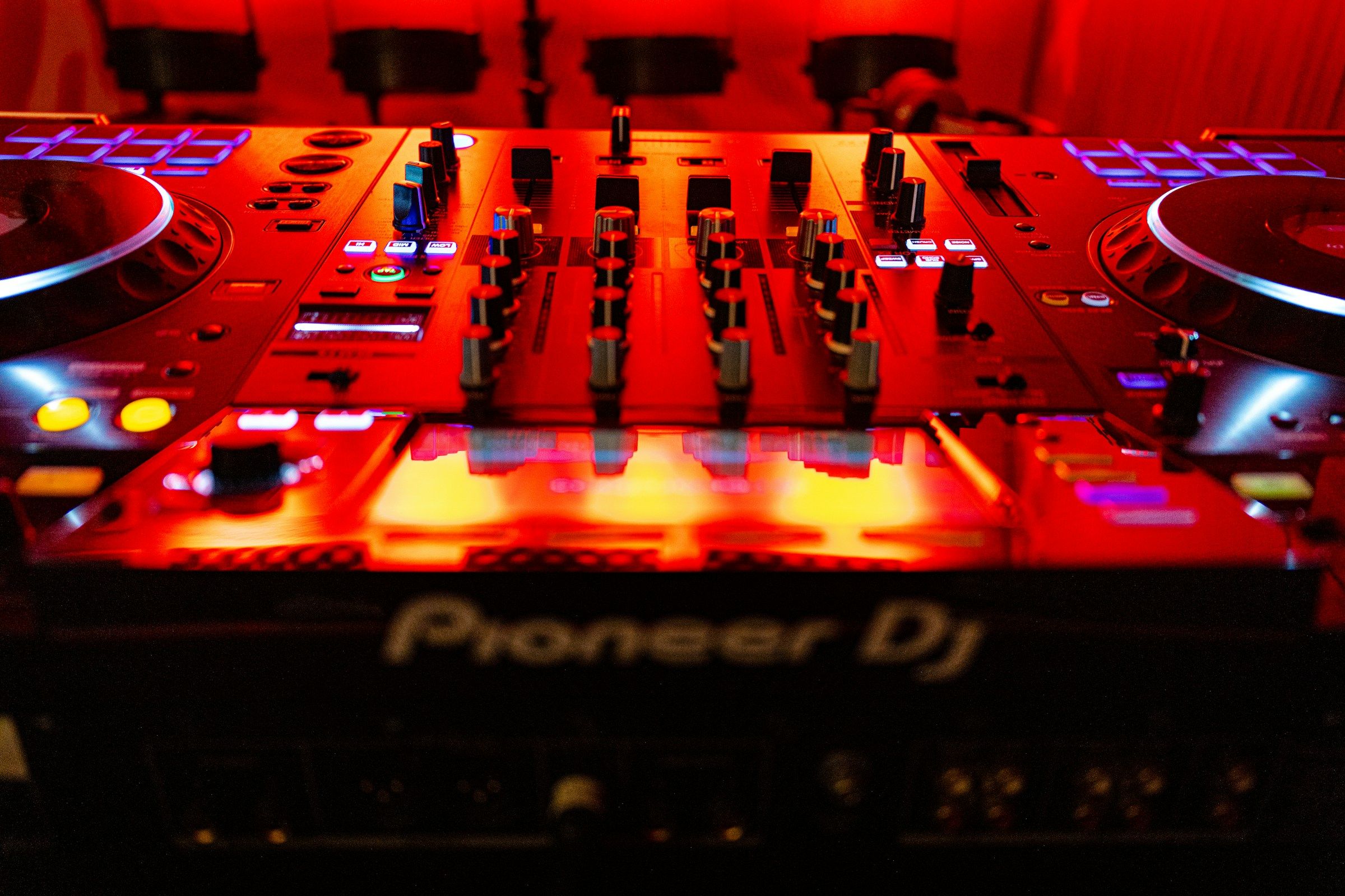 DJ equipment in a dark booth lit by a single low red light behind the decks