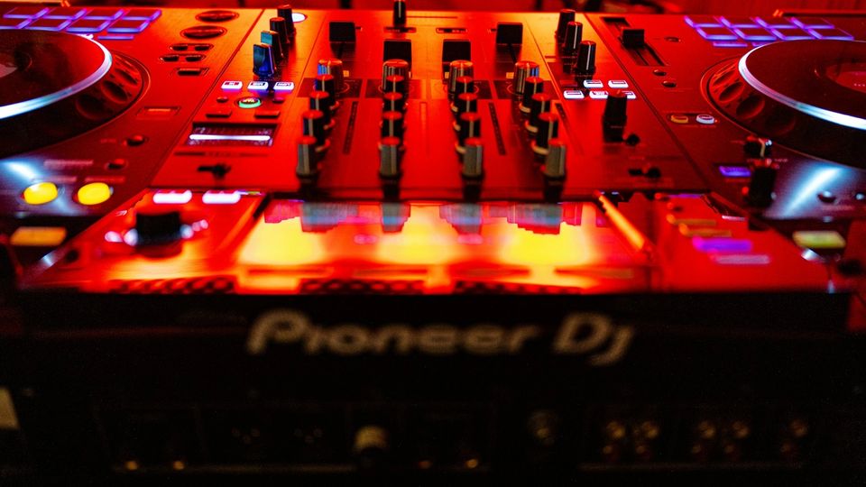 DJ equipment in a dark booth lit by a single low red light behind the decks