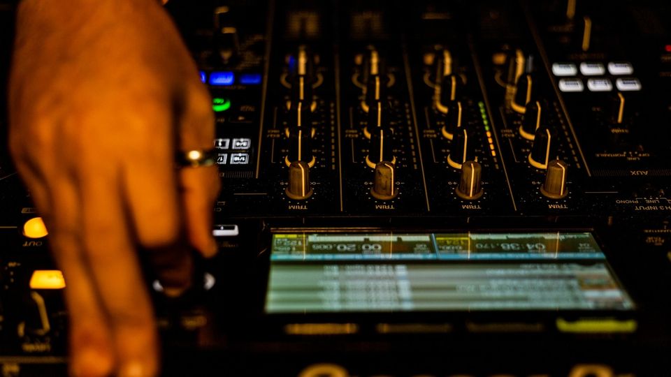 A DJ performing live in a booth with a crowd visible in the background
