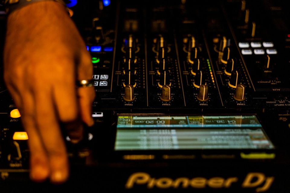 Close-up of a DJ hand adjusting a Pioneer DJ mixer in a dark booth