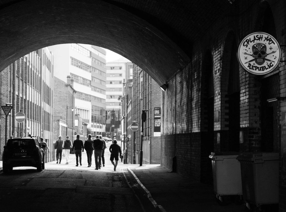 People walking under a brick archway in an industrial urban street setting