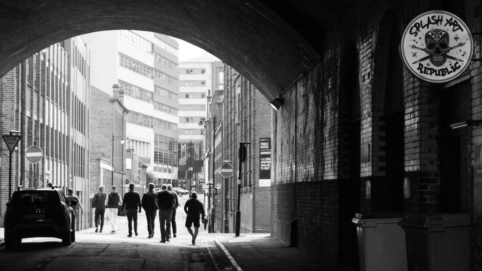 People walking under a brick archway in an industrial urban street setting