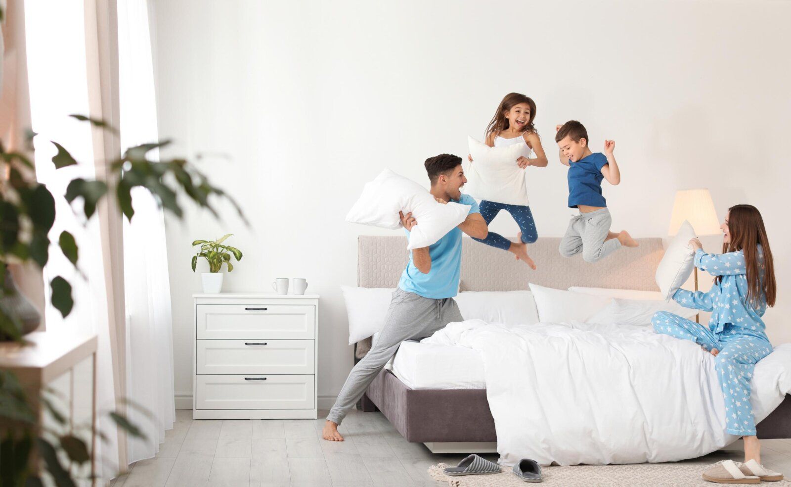 Happy family enjoying a pillow fight in a clean, pest-free bedroom with children jumping on the bed