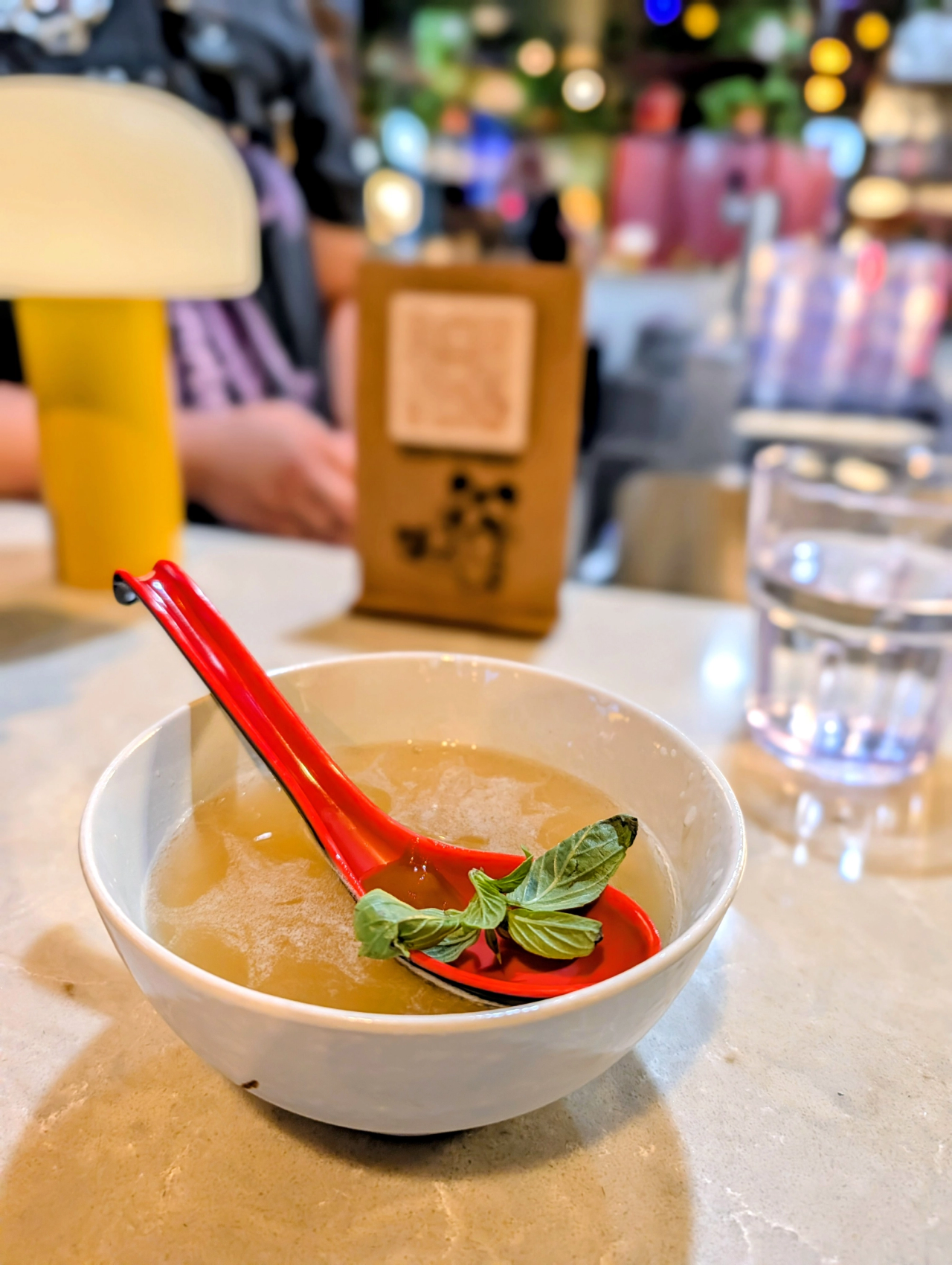 Pho-inspired cocktail served in a white bowl with a red spoon and fresh green herbs.