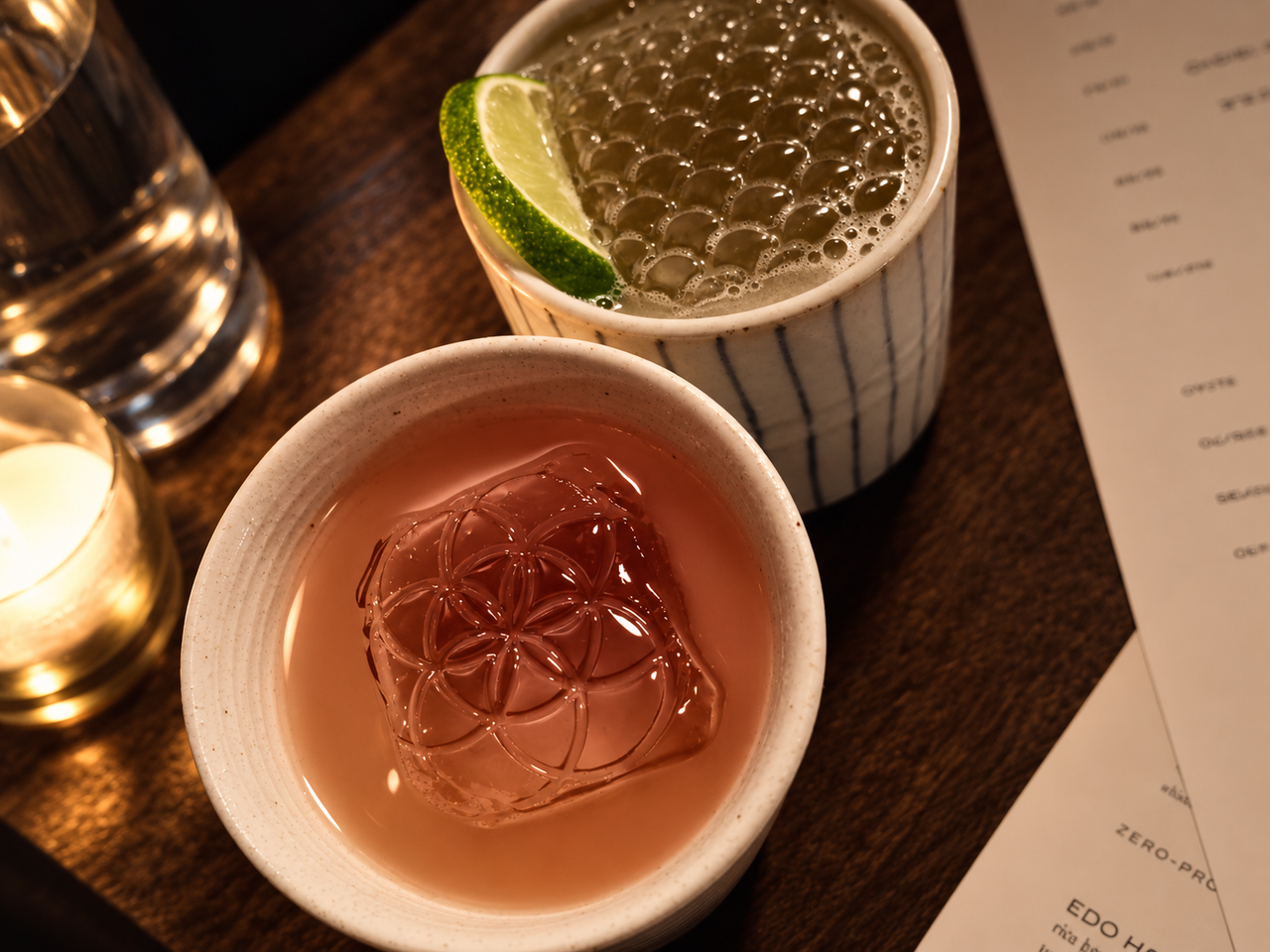 Two cocktails in ceramic cups on a candlelit wooden table at Gori Gori Peku, one with patterned ice and the other with a lime wedge