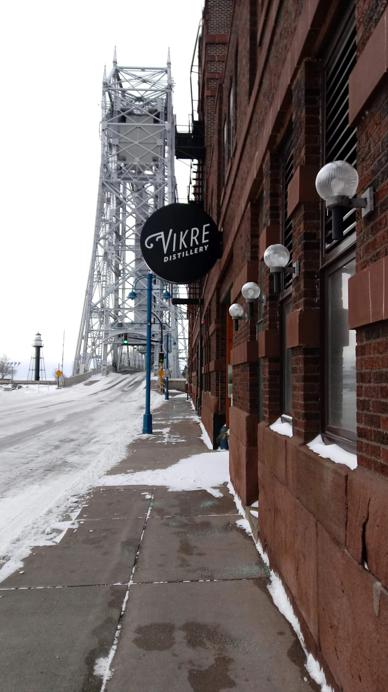 Vikre Distillery’s round sign on a snowy brick building beside Duluth’s Aerial Lift Bridge