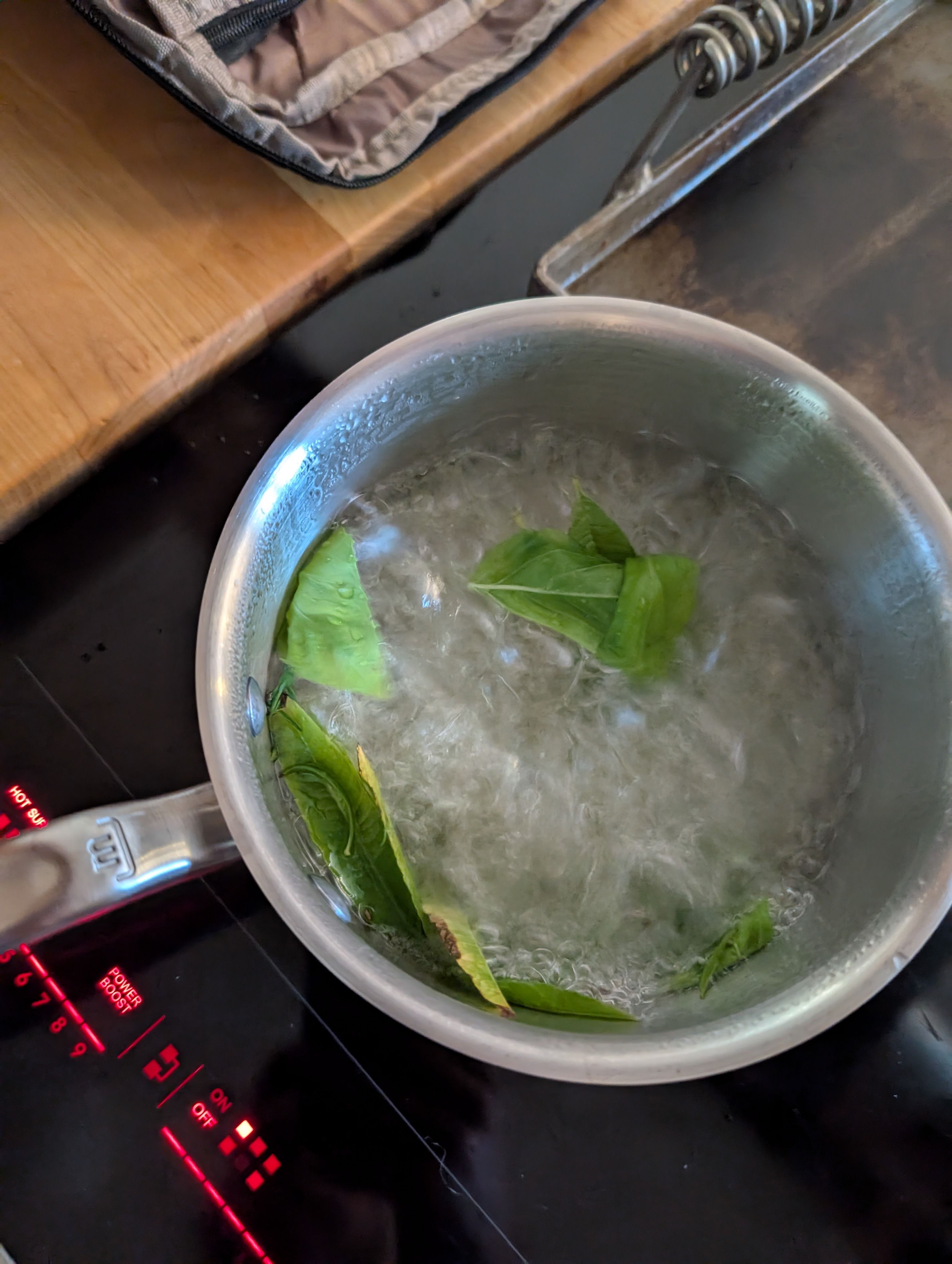 Basil leaves in boiling water in a saucepan on a stovetop.