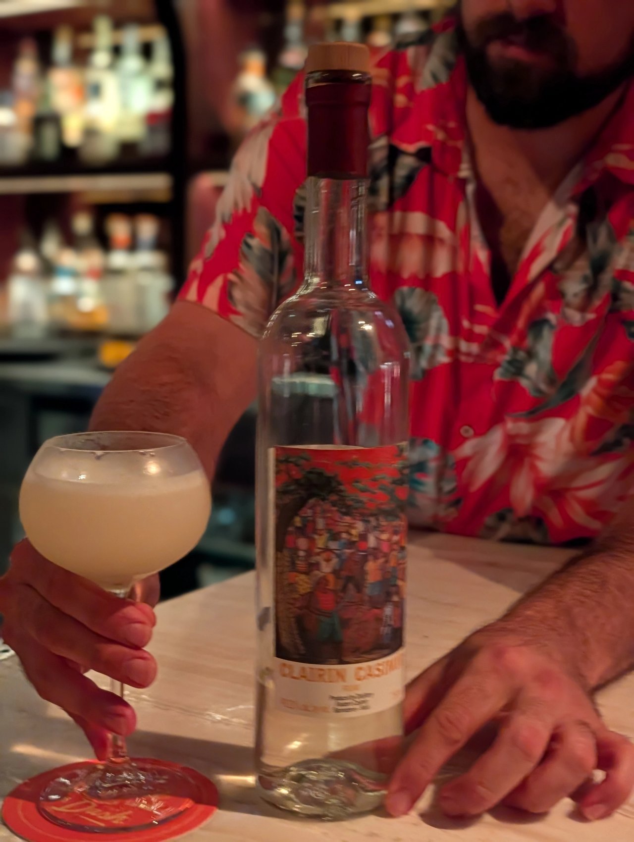 A bartender behind a rounded glass of daiquiri and a bottle of Clairin Casimir