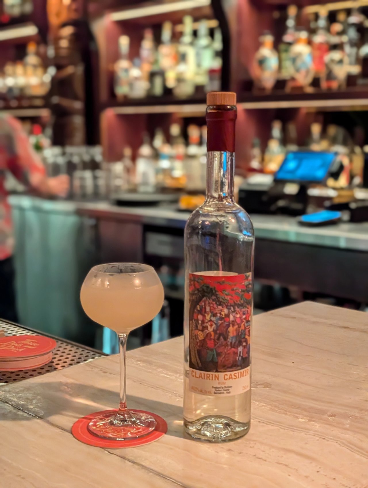 A daiquiri in a rounded stemmed glass beside a bottle of Clairin Casimir on the bar