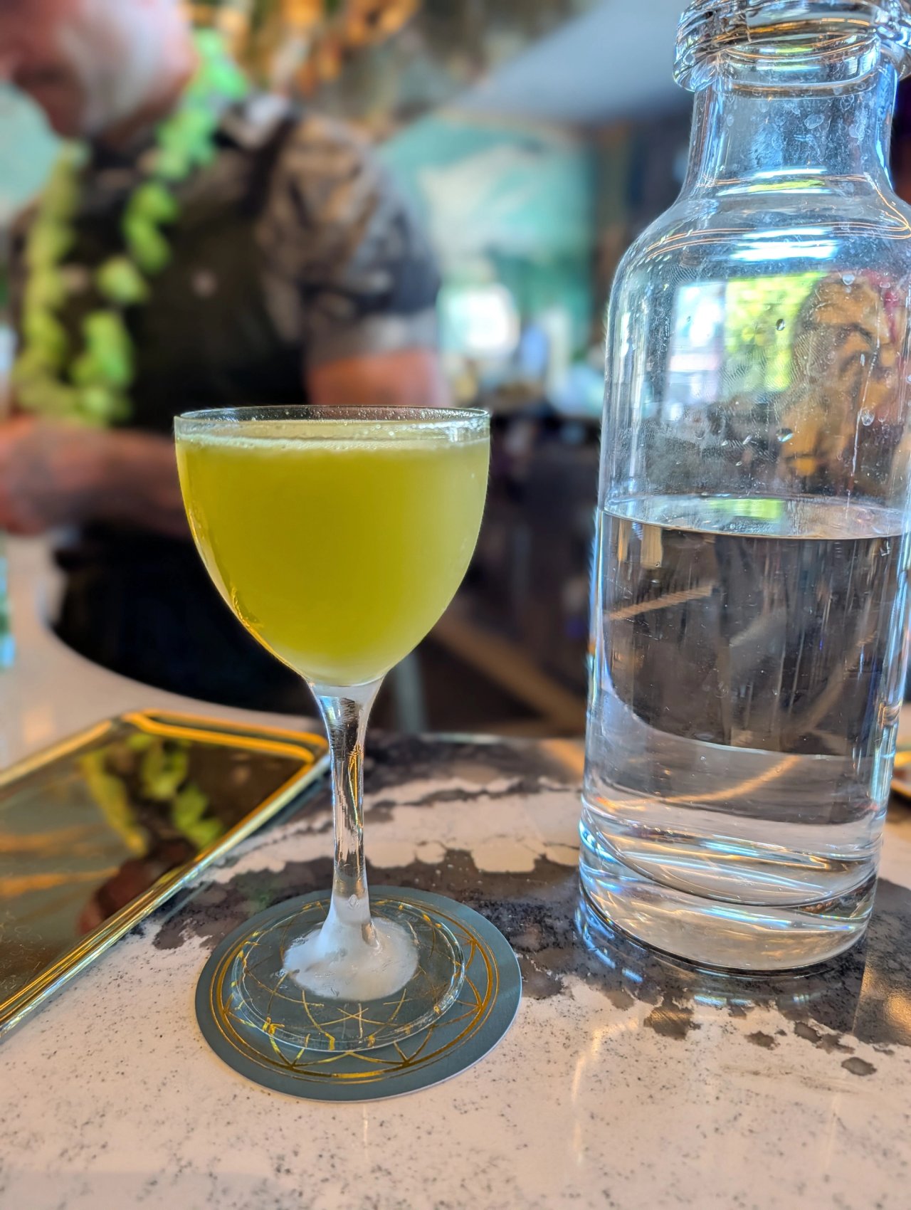 A vivid green sour in a stemmed glass on the Kingfisher bar, beside a water bottle
