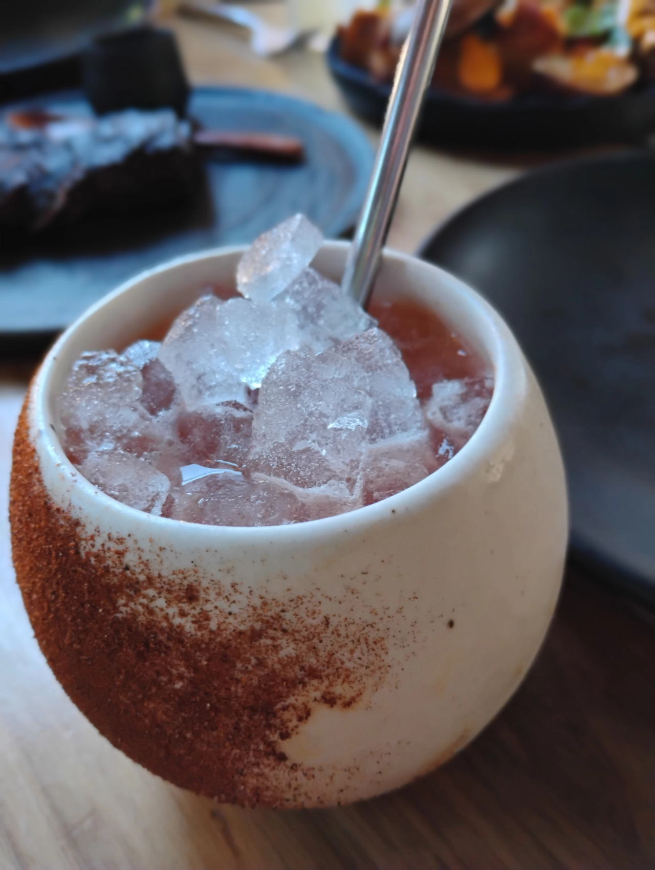 A pink cocktail over crushed ice in a white ceramic cup with a spice-coated side at Porzana