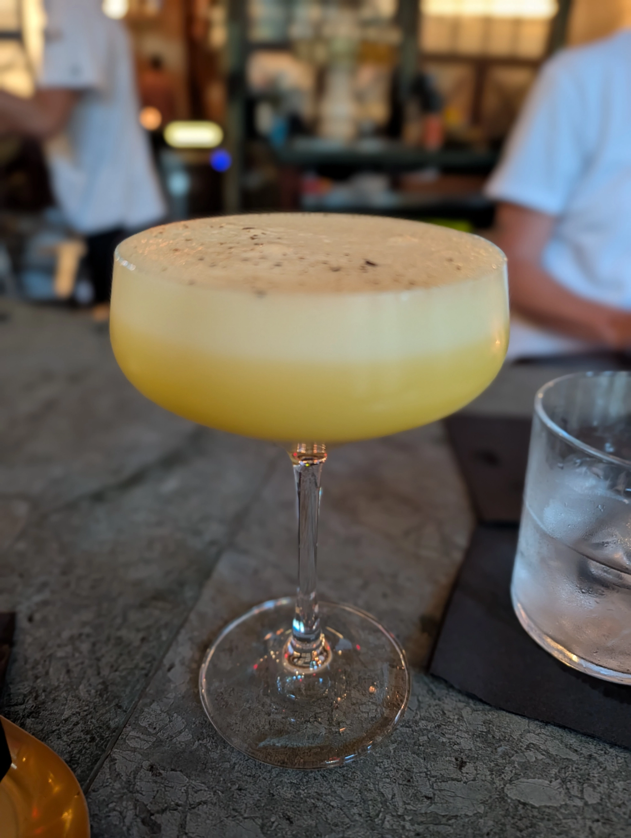 Pale yellow cocktail in a coupe glass with a thick foamy top at Fives.