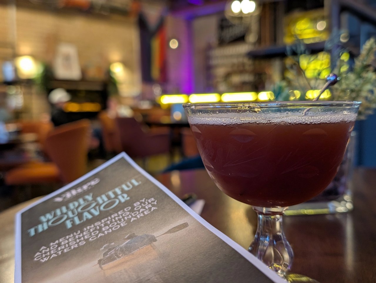 A dark red cocktail in an etched coupe beside a Vikre menu in the warmly lit tasting room