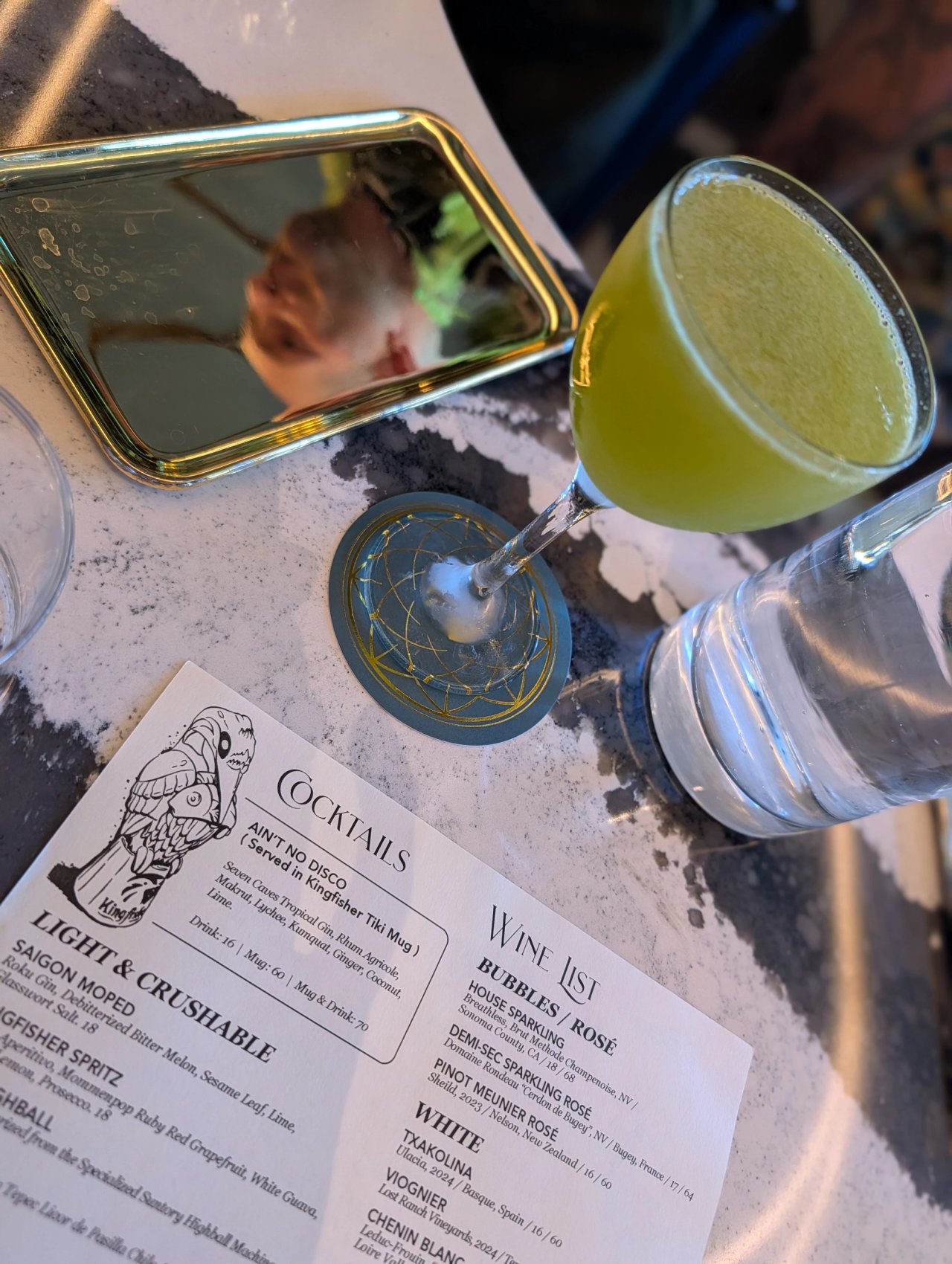 An overhead view of the green fish-sauce cocktail beside the Kingfisher cocktail menu