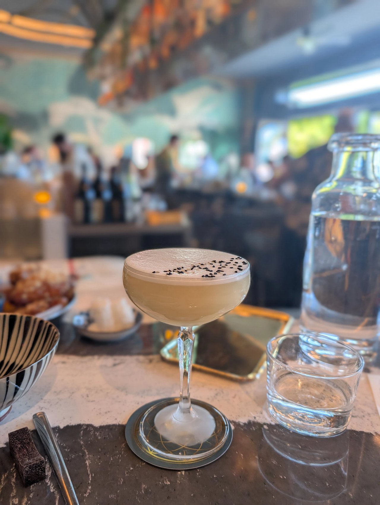 A pale cocktail in a coupe with a foam cap and black sesame seeds at Kingfisher