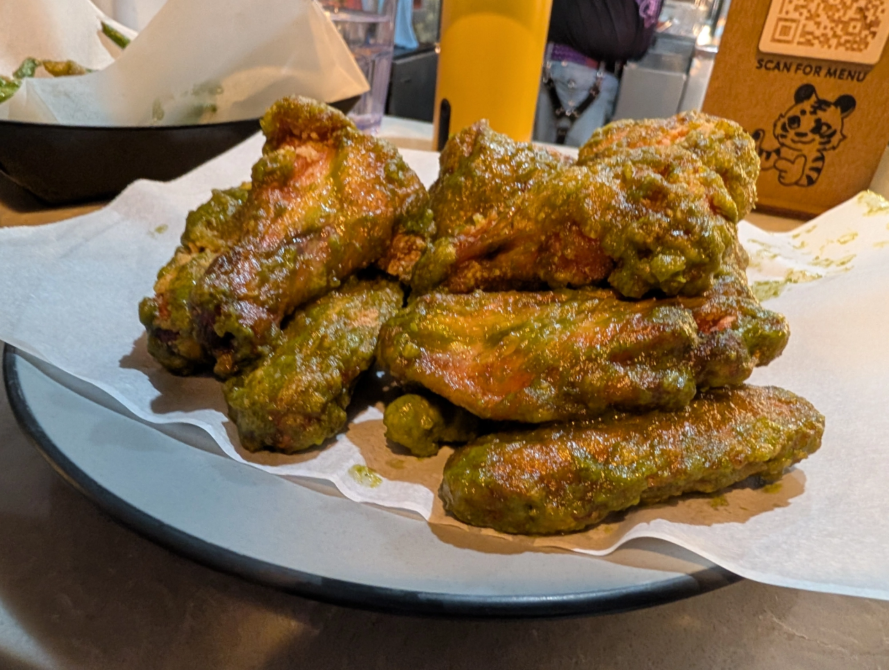 Plate of chicken wings coated in a green sauce on parchment paper.