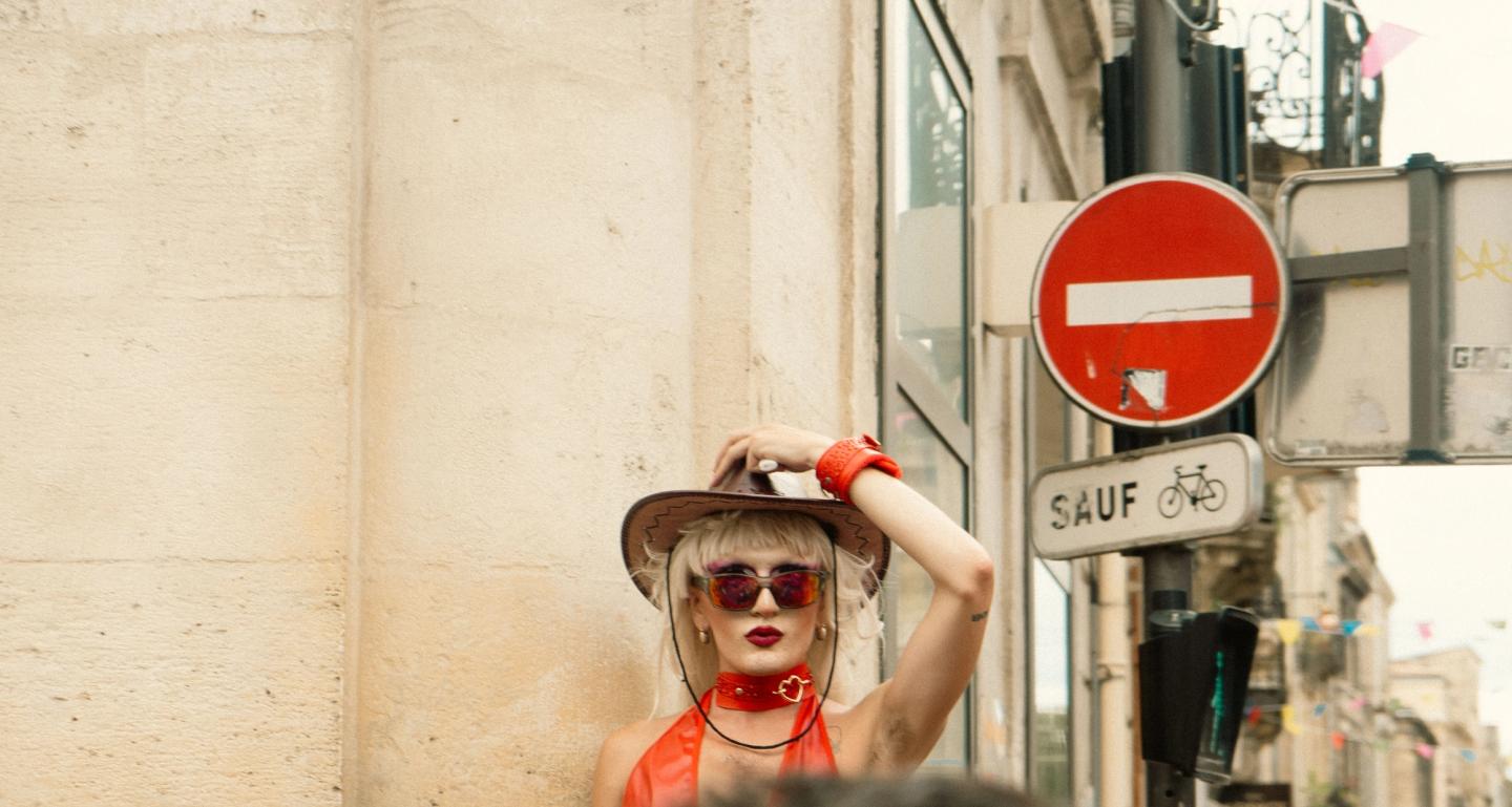 A drag queen holding her hat in the city streets