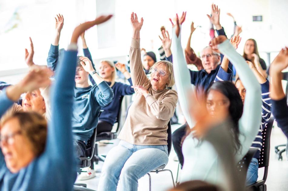 Eldre og VGS-elever synger og trimmer sammen i klasserommet.
