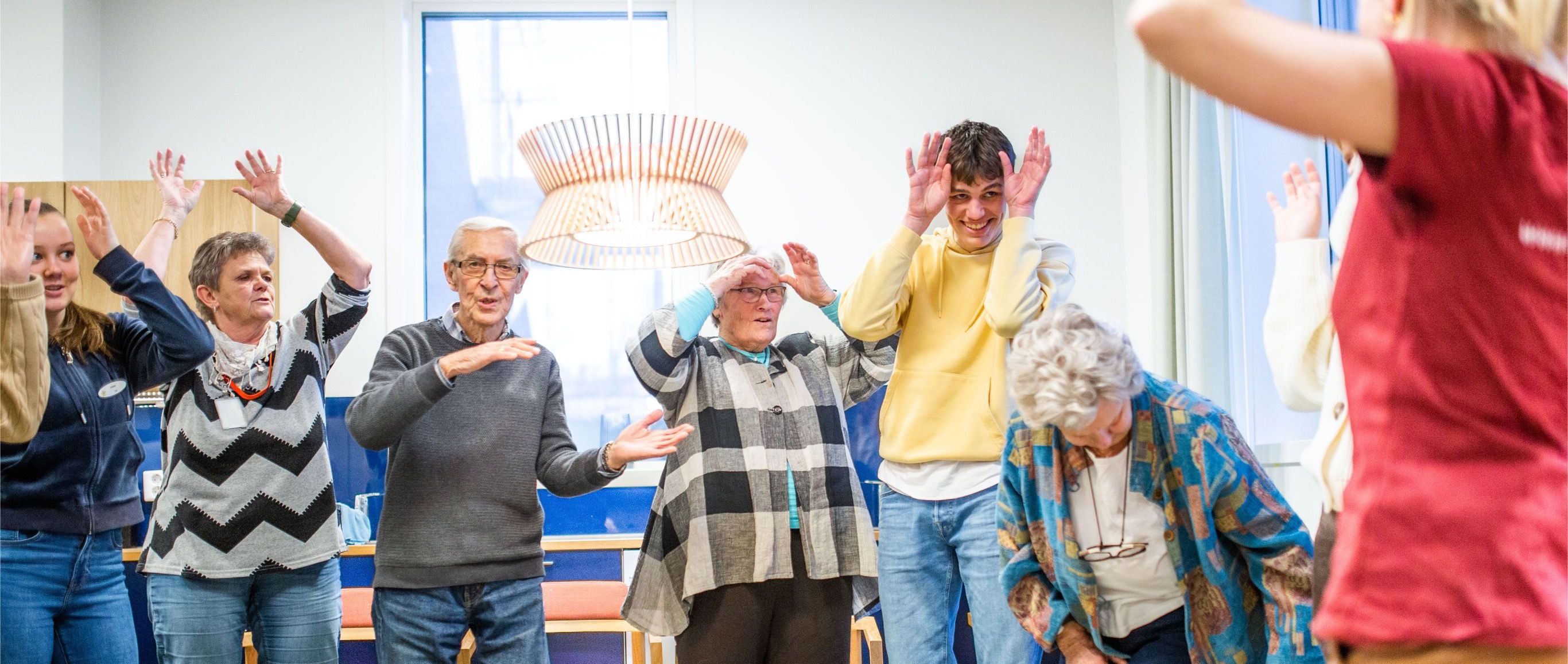 En ung VGS-elev danser og ler sammen med en voksen kvinne og en eldre mann på en syngende institusjon