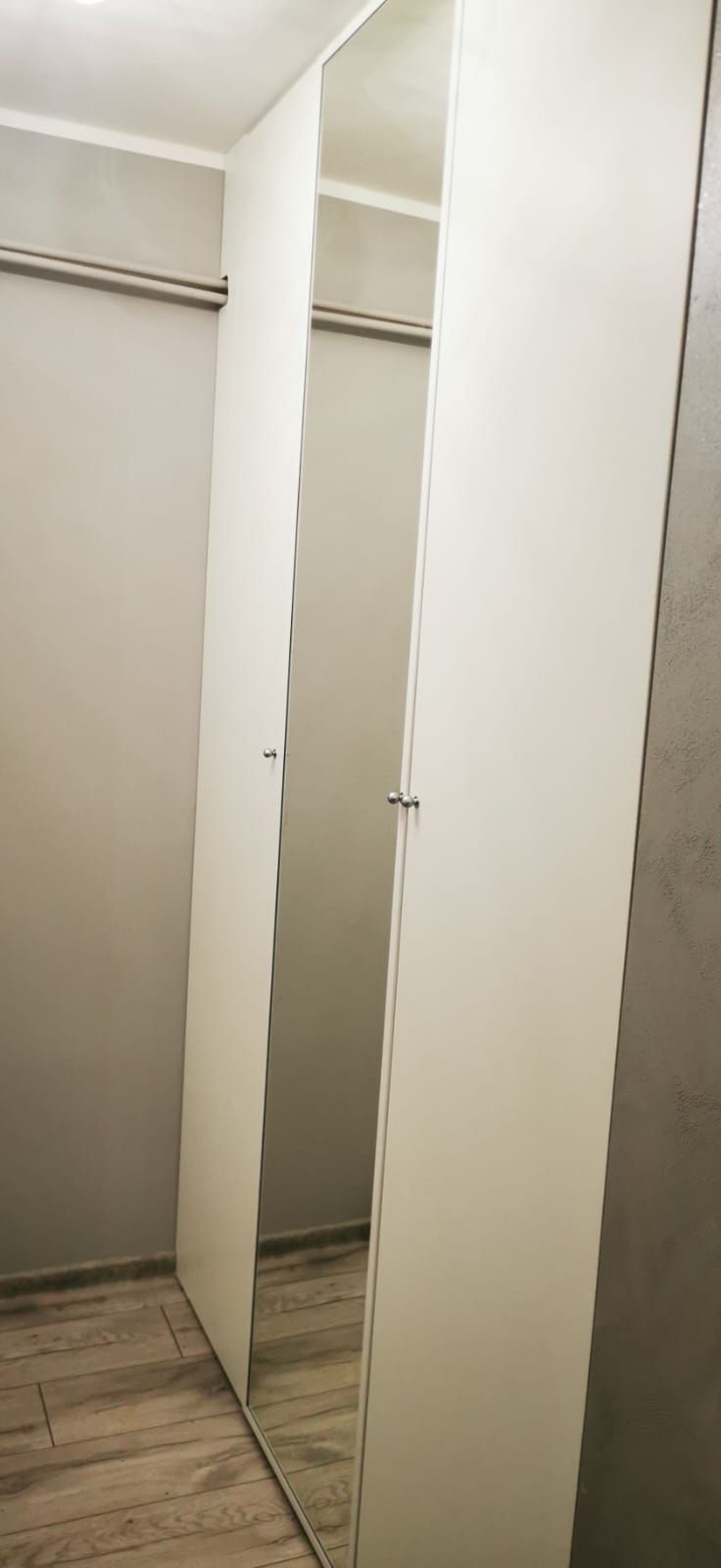 Biała szafa dwudrzwiowa z lustrzanym frontem i drążkiem w środku