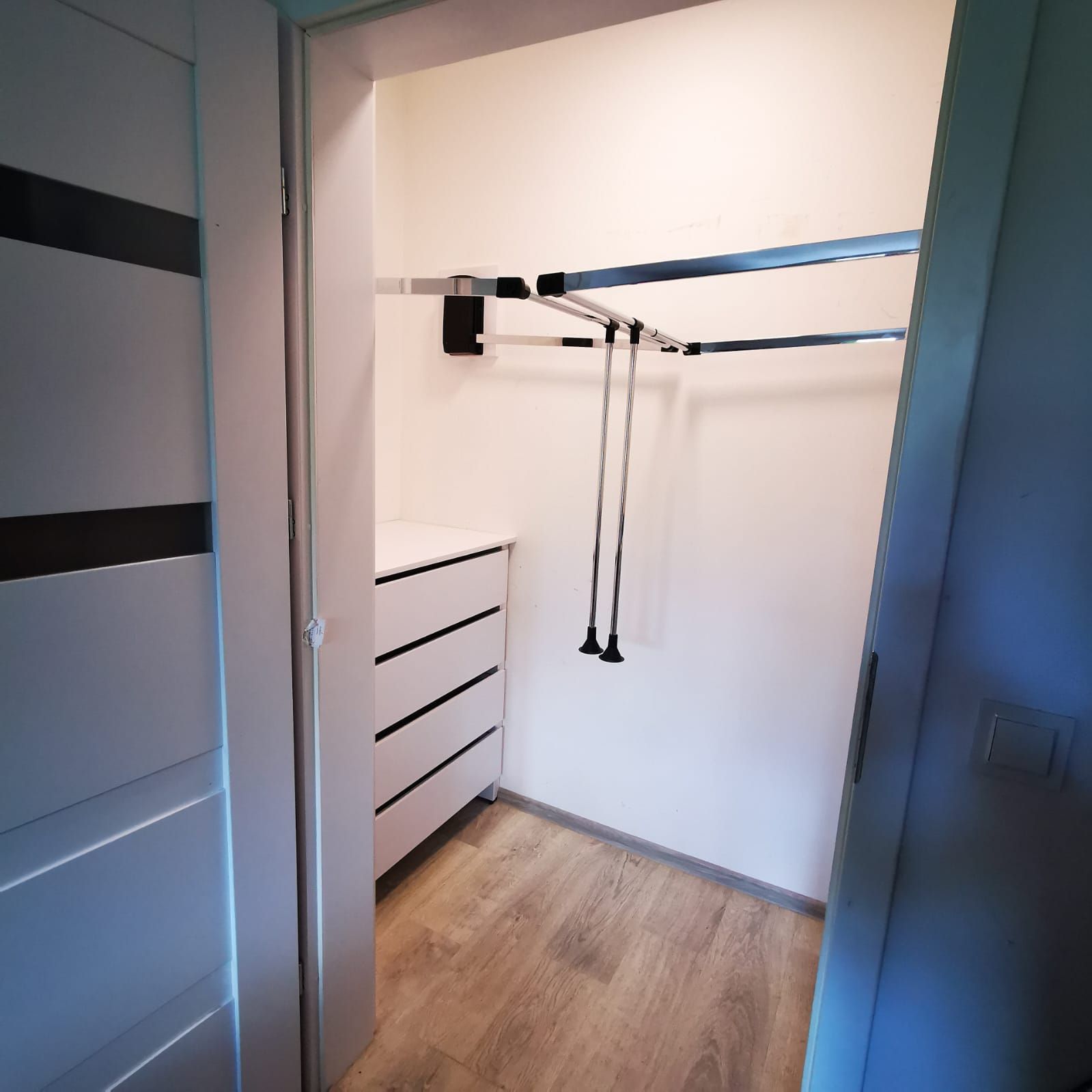 Garderoba walk-in z białą komodą i chromowanymi drążkami, drzwi przesuwne