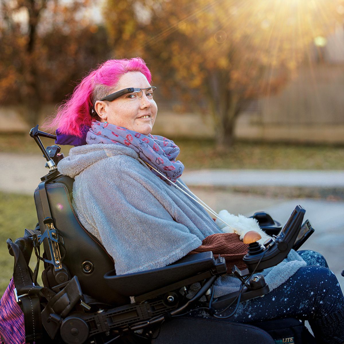 Munevo-Nutzerin mit rosa Haaren die lächelnd in ihrem Rollstuhl sitzt