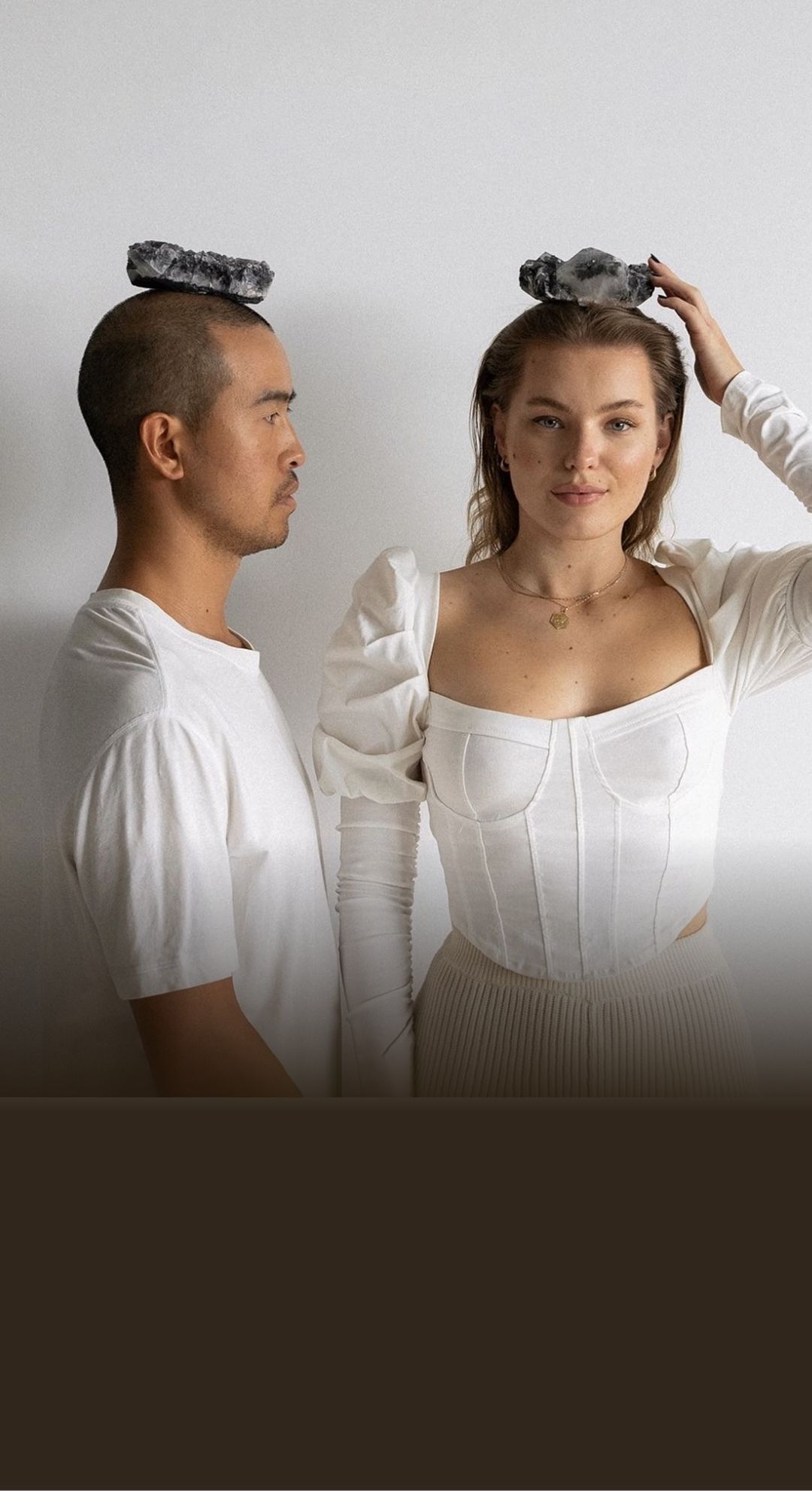 portrait of a man and woman in white shirts balancing crystals on their head