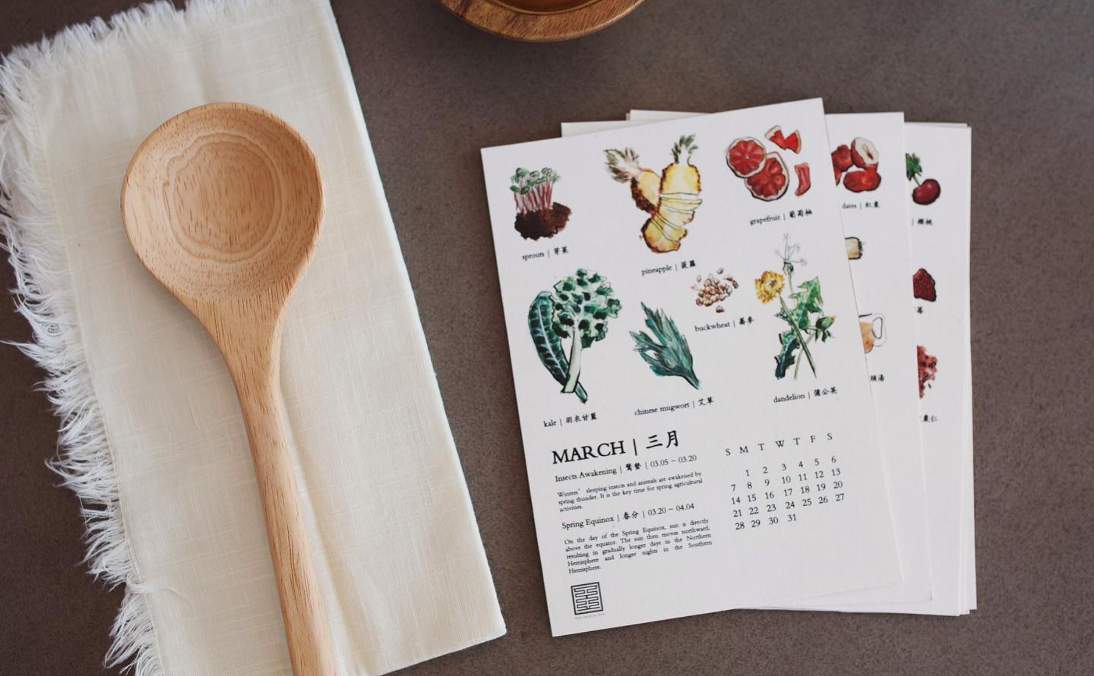 Seasonal eating calendar with watercolour illustrations of food items, placed next to a wooden spoon