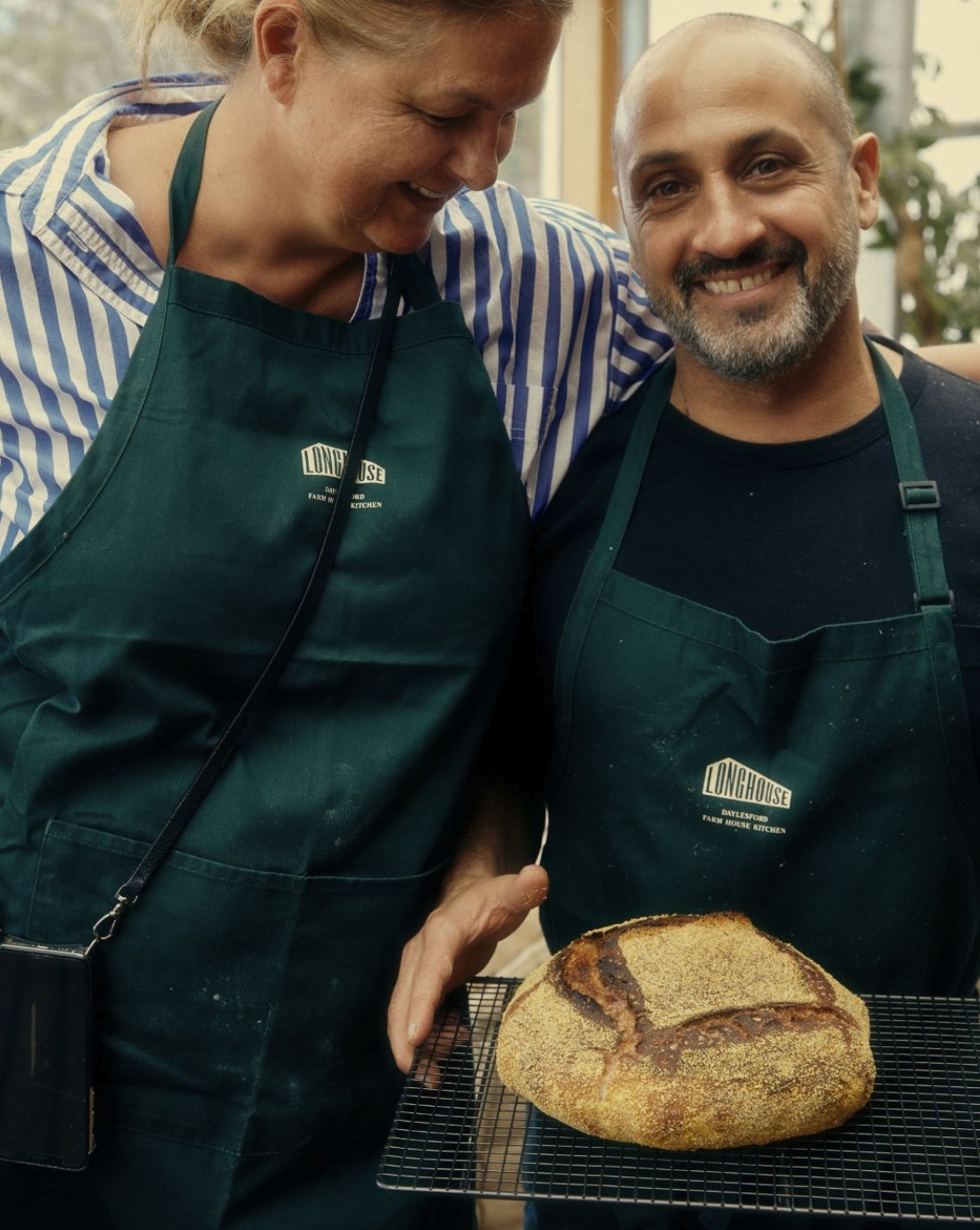 Smiling man and woman in green aprons holding a fresh baked sourdough