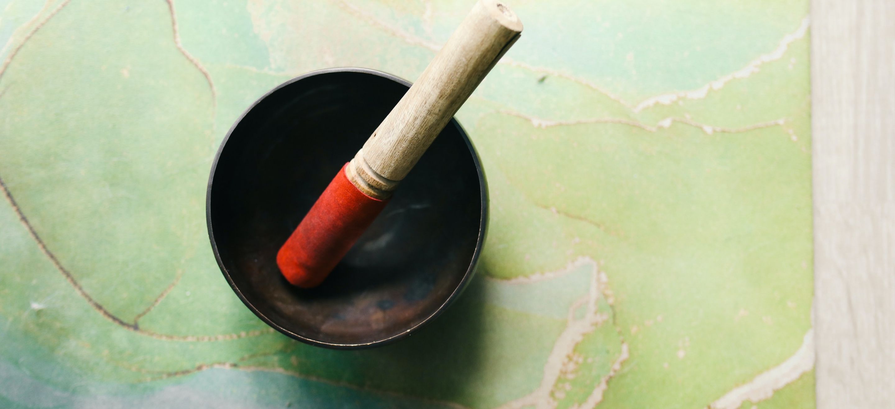 Singing bowl with mallet with red tip on a green and blue marble surface
