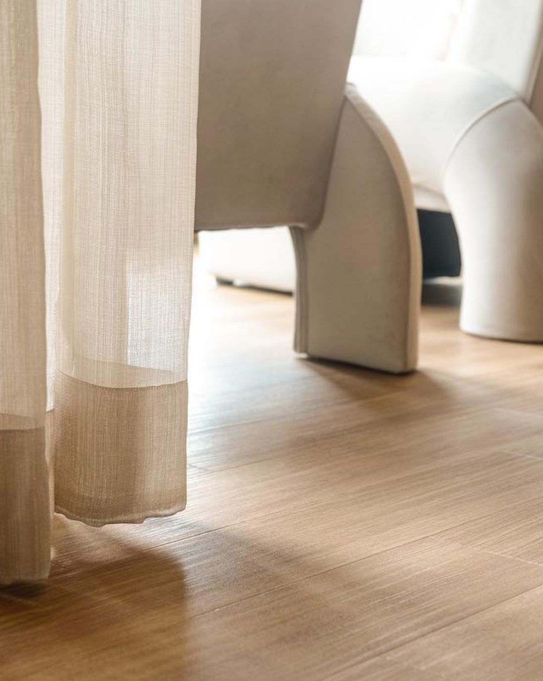 Closeup shot of beige interior details of wooden floor, sheer beige curtains and leg of armchairs