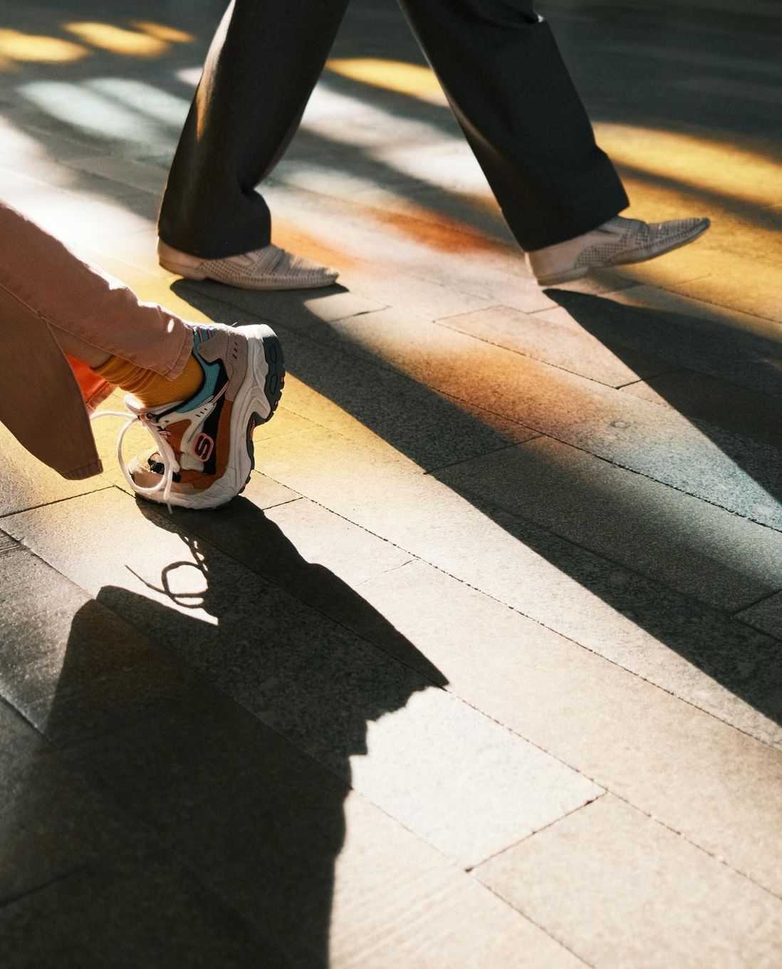 2 sets of legs and feet walking, casting a long shadow on sidewalk