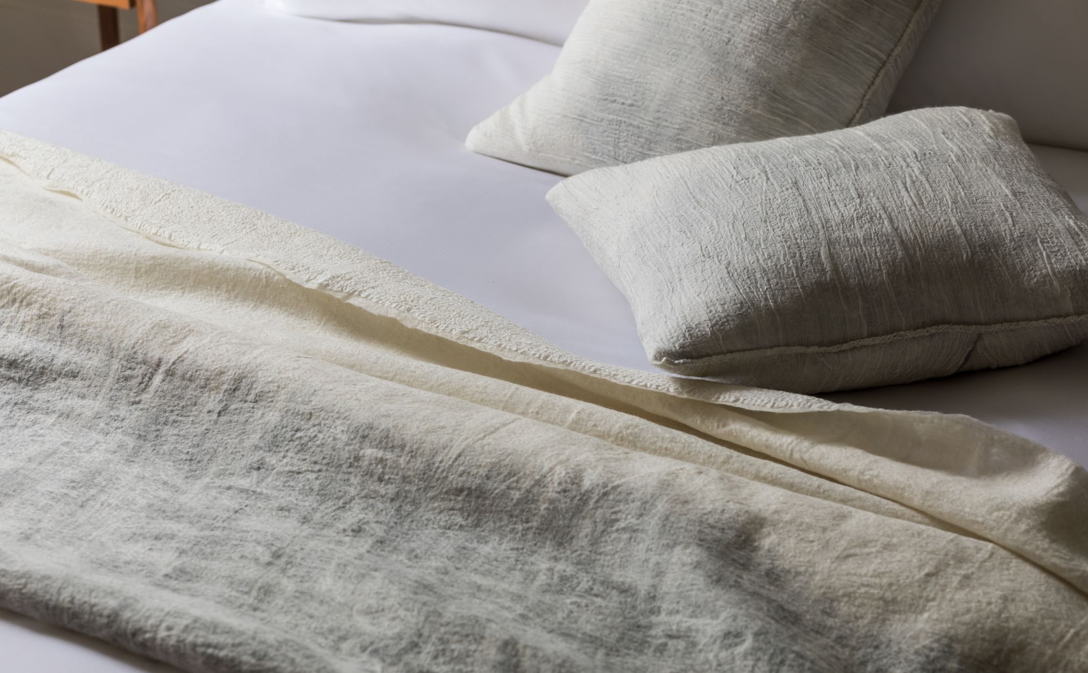 A closeup of bed with textured comforter and shams on white sheets
