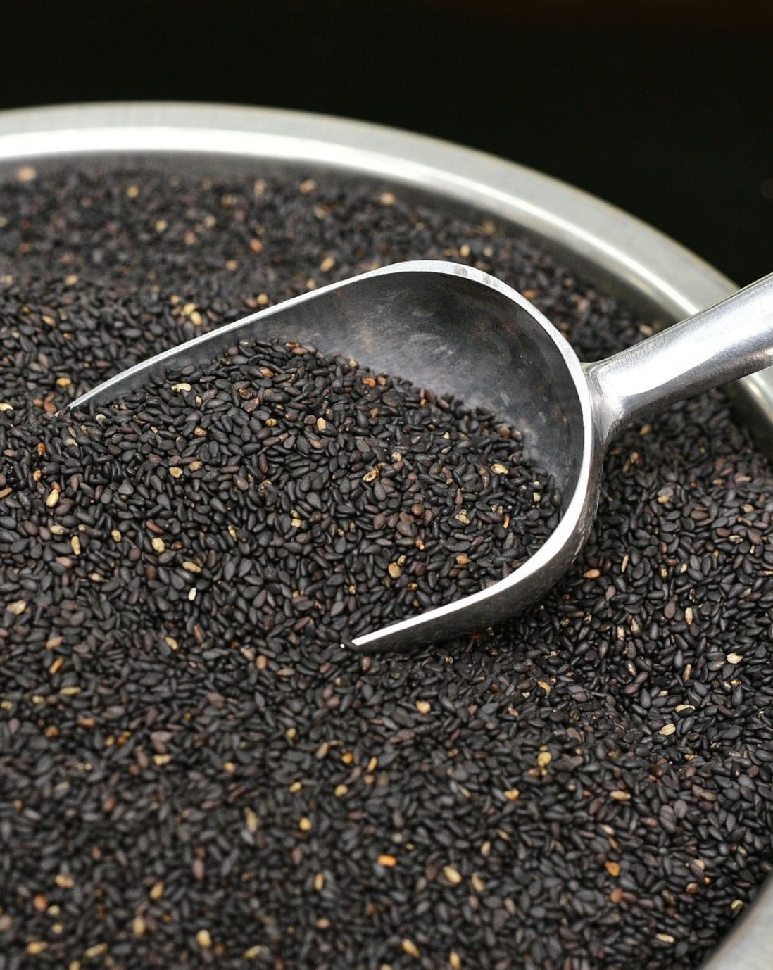 Close up of black sesame seeds in a meal bowl with scooping spoon