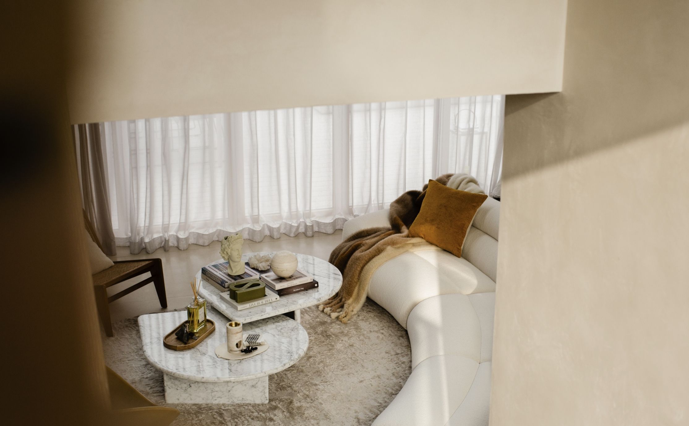 Living room space with 2 white marble coffee tables and a curved white couch 