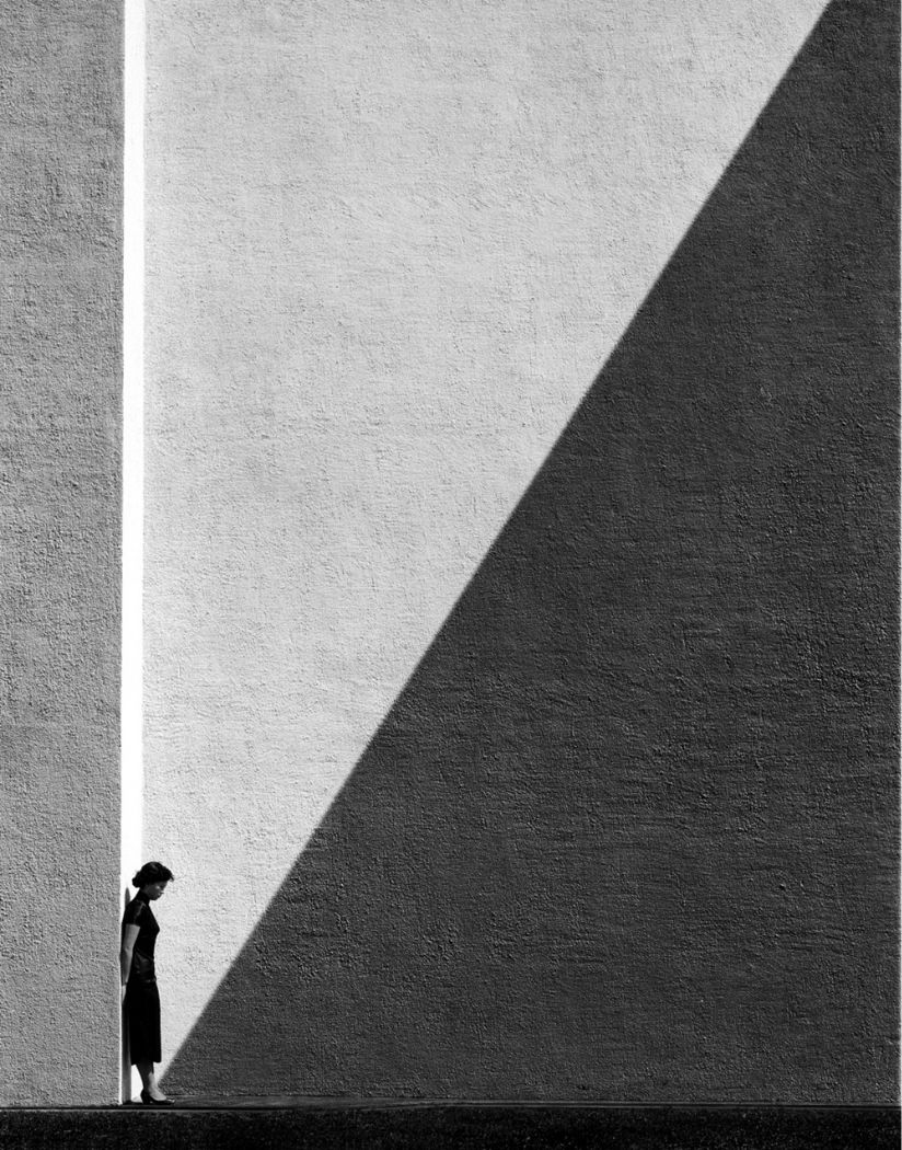 Woman standing against a column on a vast wall with a stark diagonal shadow, Approaching Shadow by Fan Ho