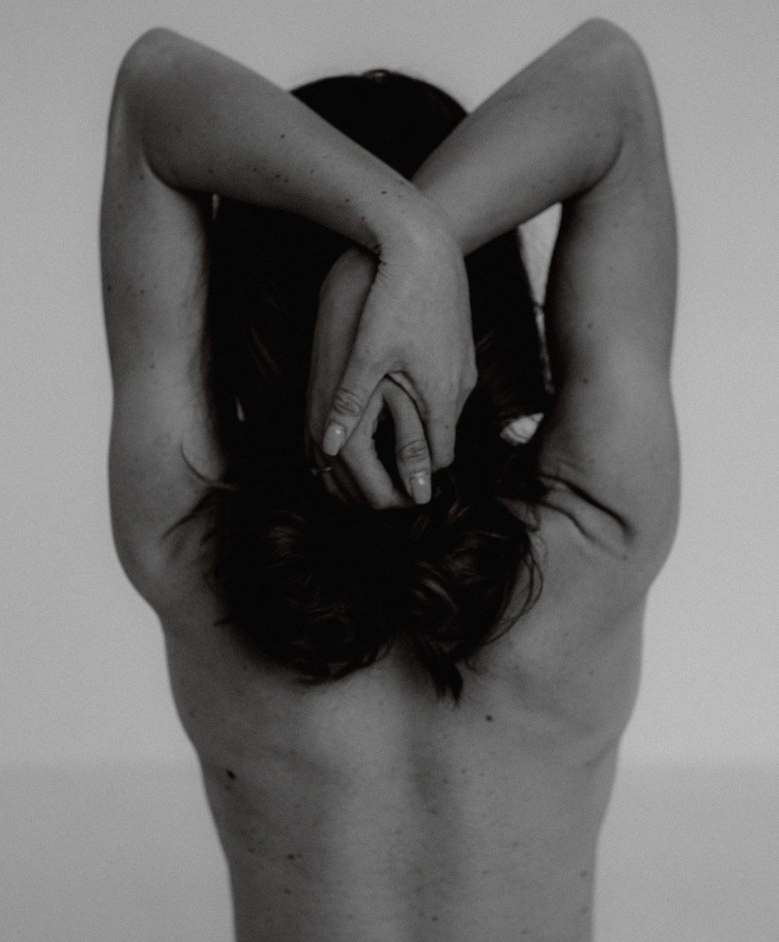 Black and white image of topless woman’s back with her hands over her head 