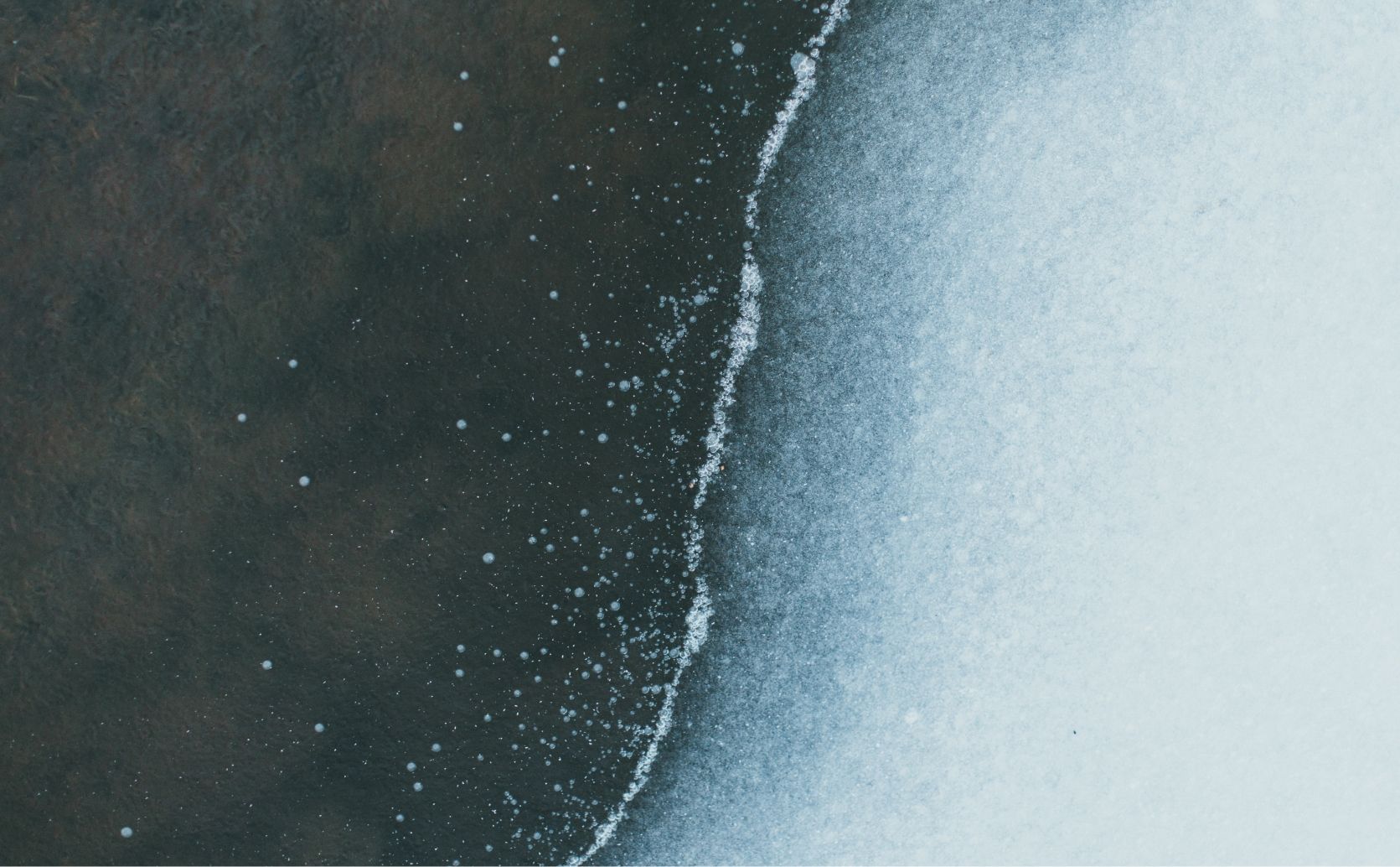 Abstract aerial photo of a body of water, half frosty and frozen, and half murky speckled with frozen air bubbles