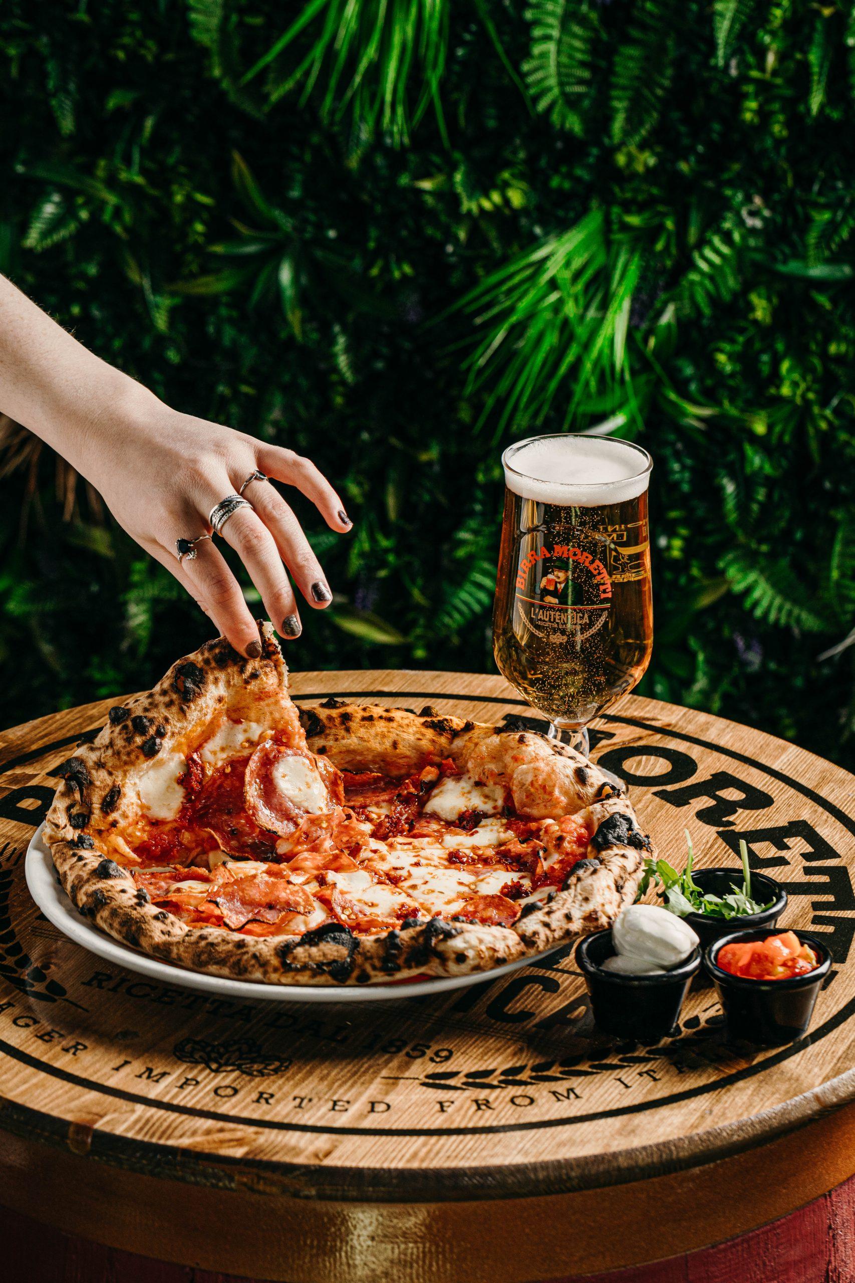 A pizza and a beer on a barrel table