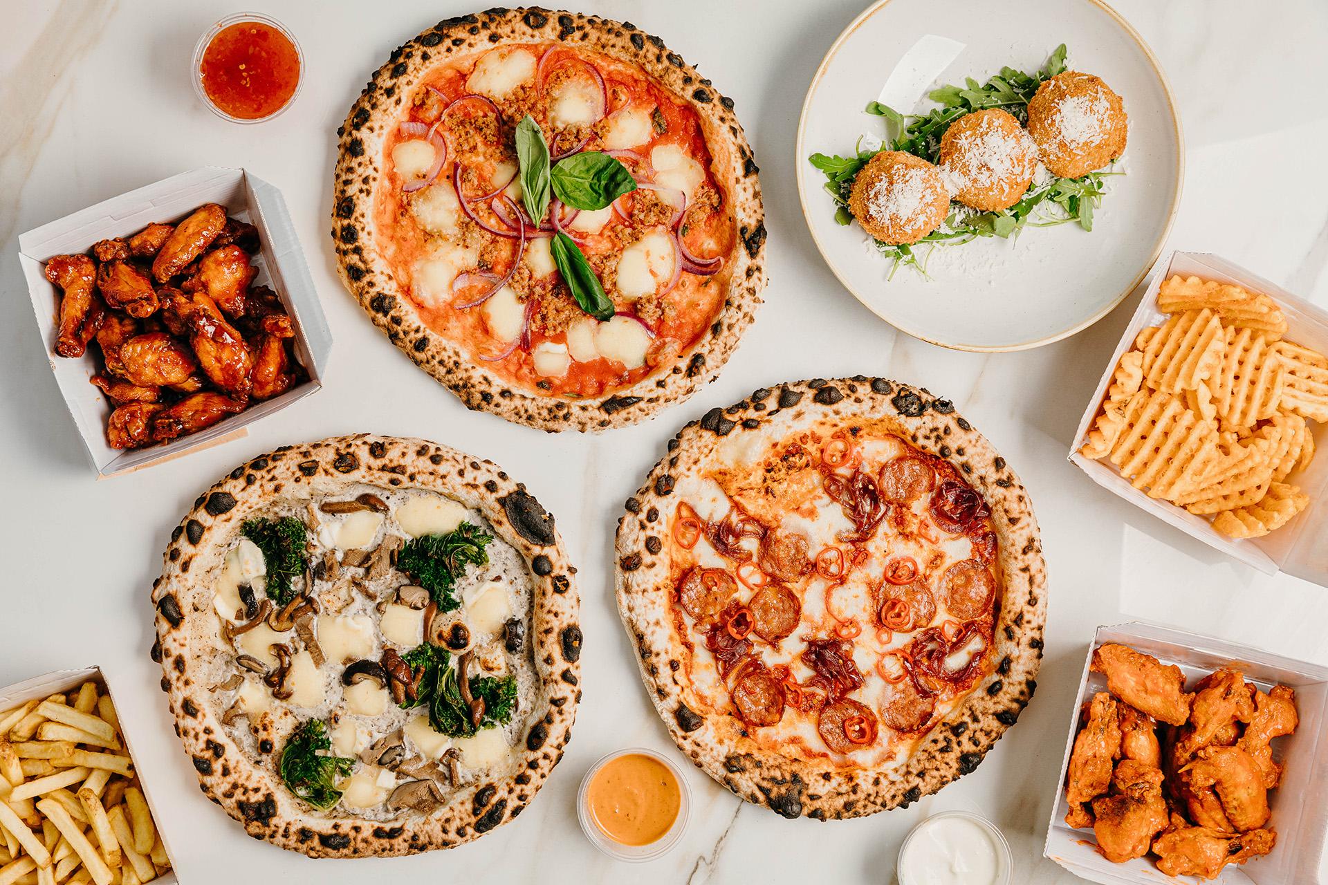 A spread of Fired Up pizzas, wings, arancini and waffle chips on a white table
