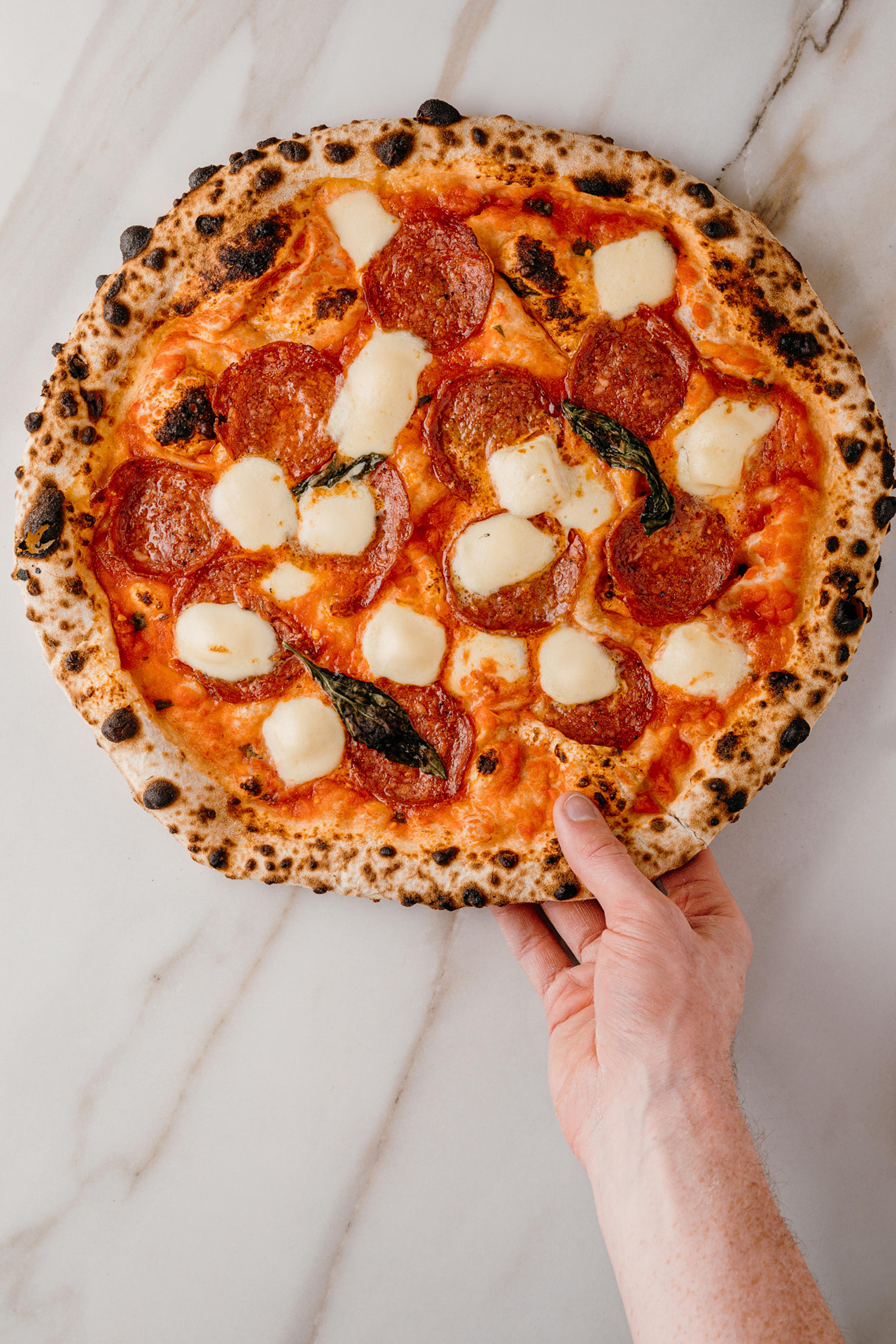 A wood-fired pizza held over a marble counter