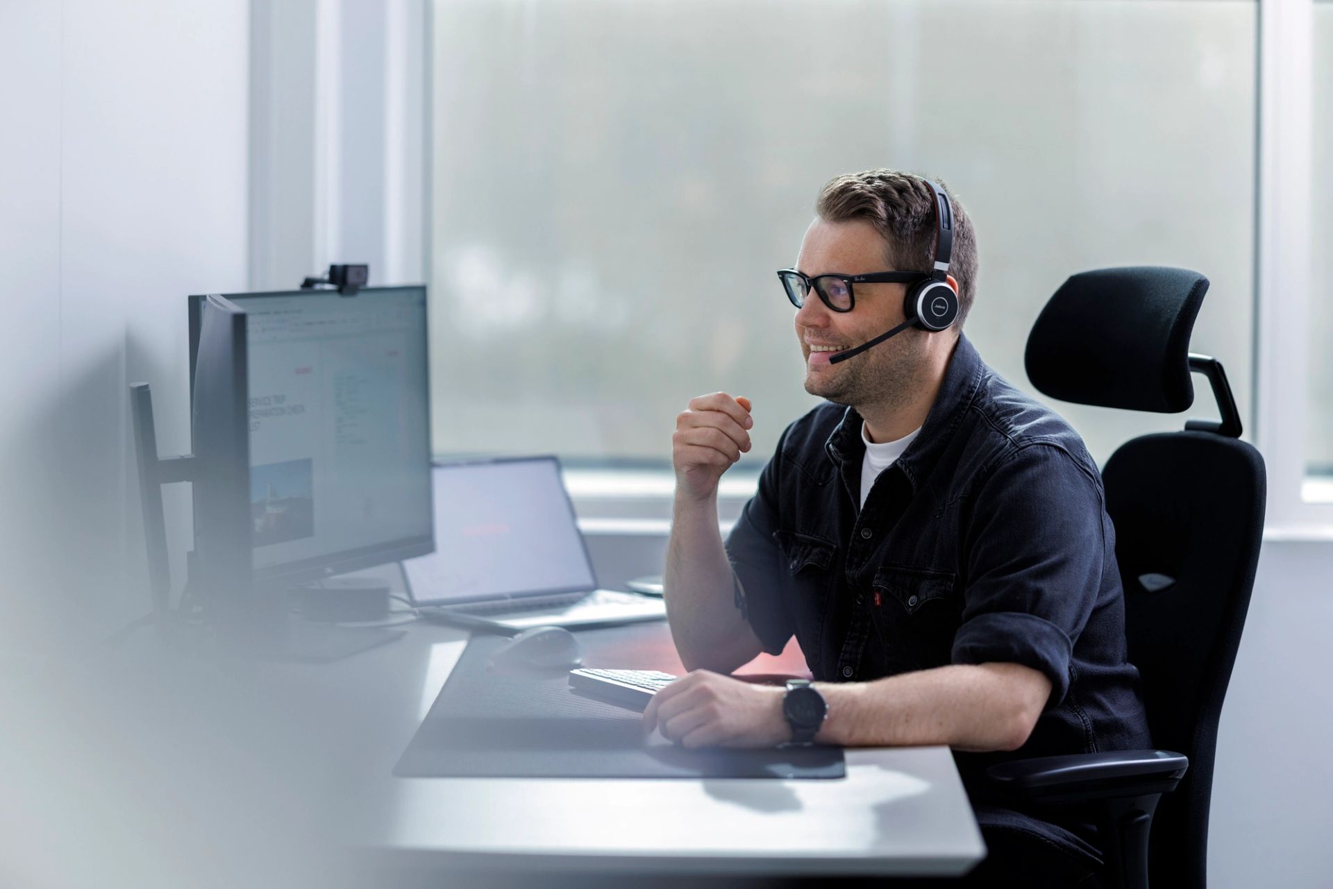 Smiling employee wearing a headset at his desk with dual monitors, ready to assist customers